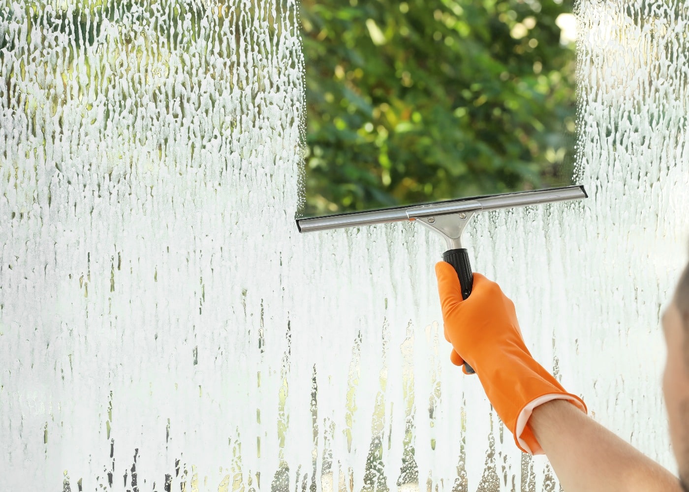 Male janitor cleaning window with squeegee, closeup